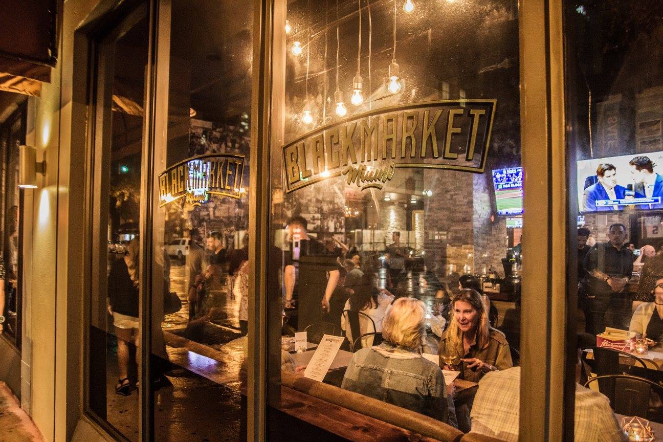 BLACKMARKET Miami storefront at night — gold window lettering with diners inside