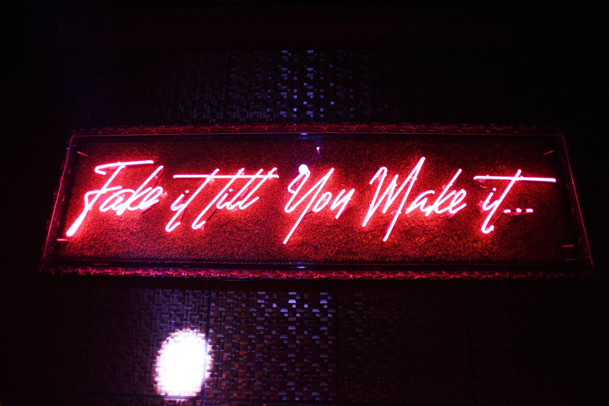 'Fake it till you make it' neon over the woven wall