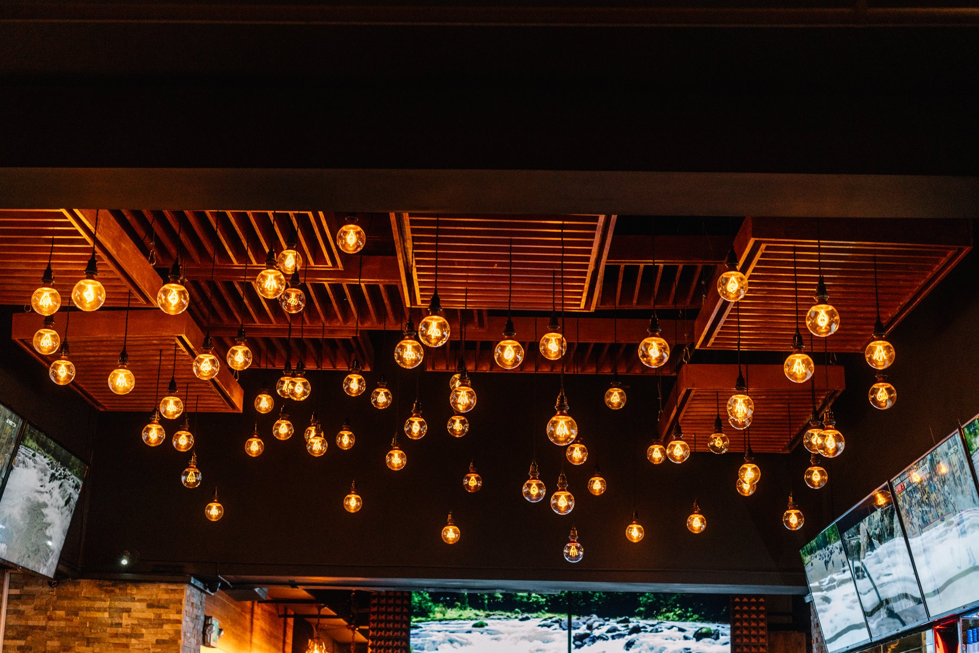 Edison-bulb canopy suspended from the wood-slat ceiling
