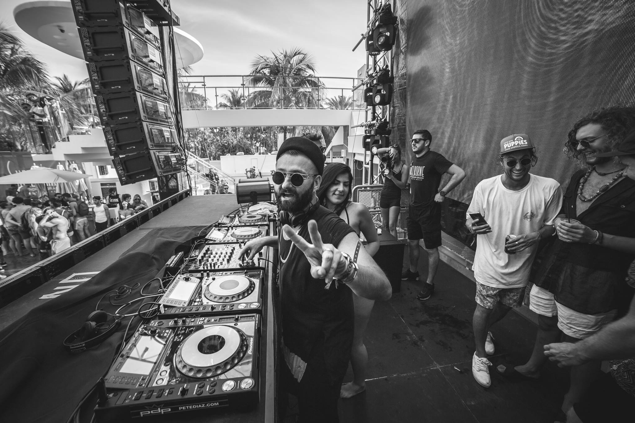 Black and white shot of a DJ flashing a peace sign at the booth during a daytime pool set