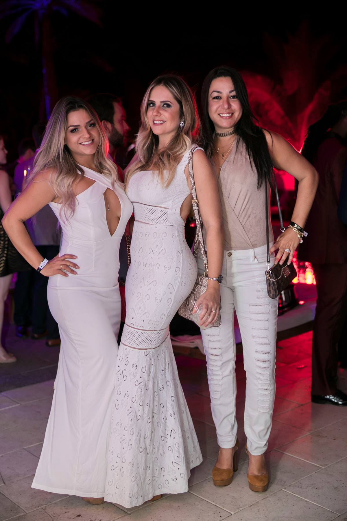 Three guests in all-white formalwear posing together under warm red light