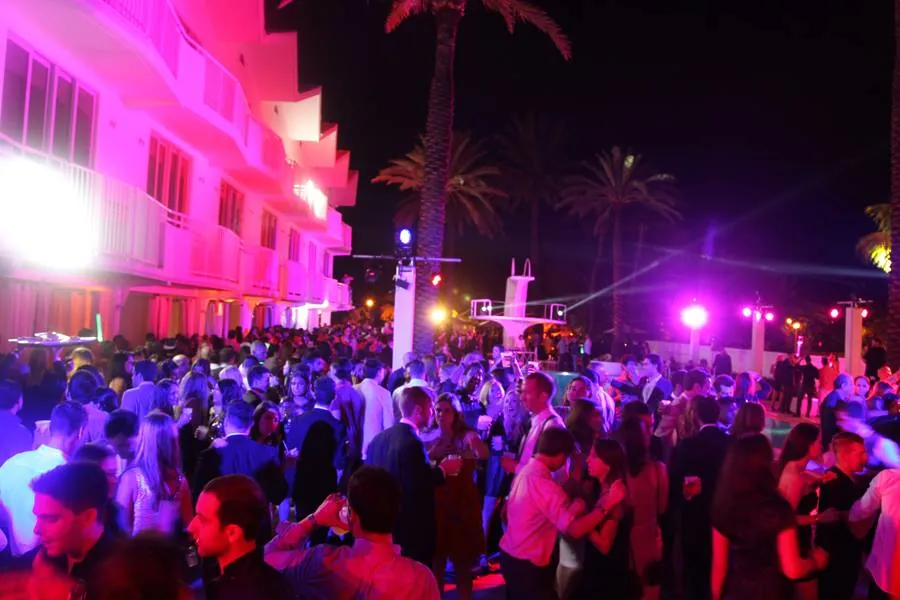 Packed Delano pool deck at night with the hotel facade washed in hot pink
