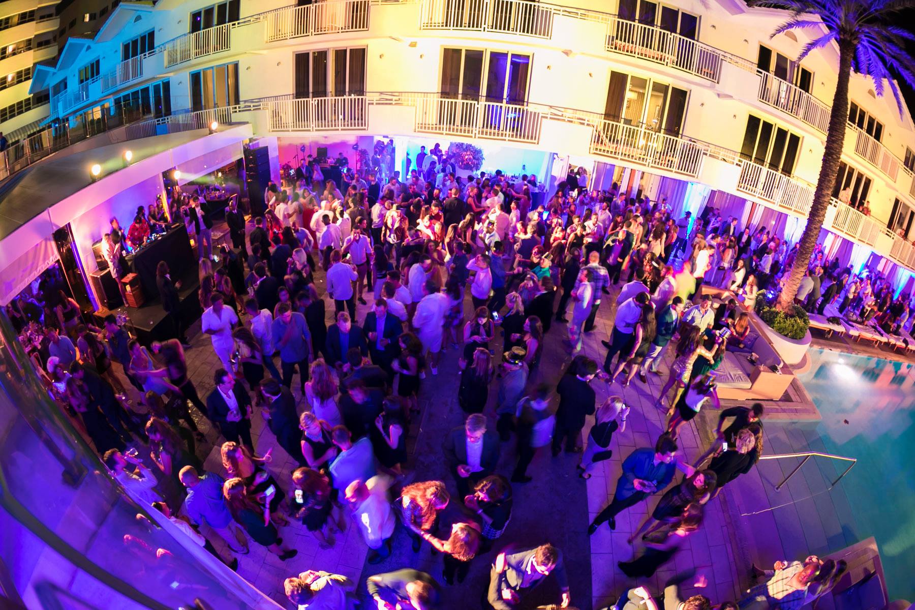 Wide fisheye of the pool party crowd beneath the floodlit hotel facade