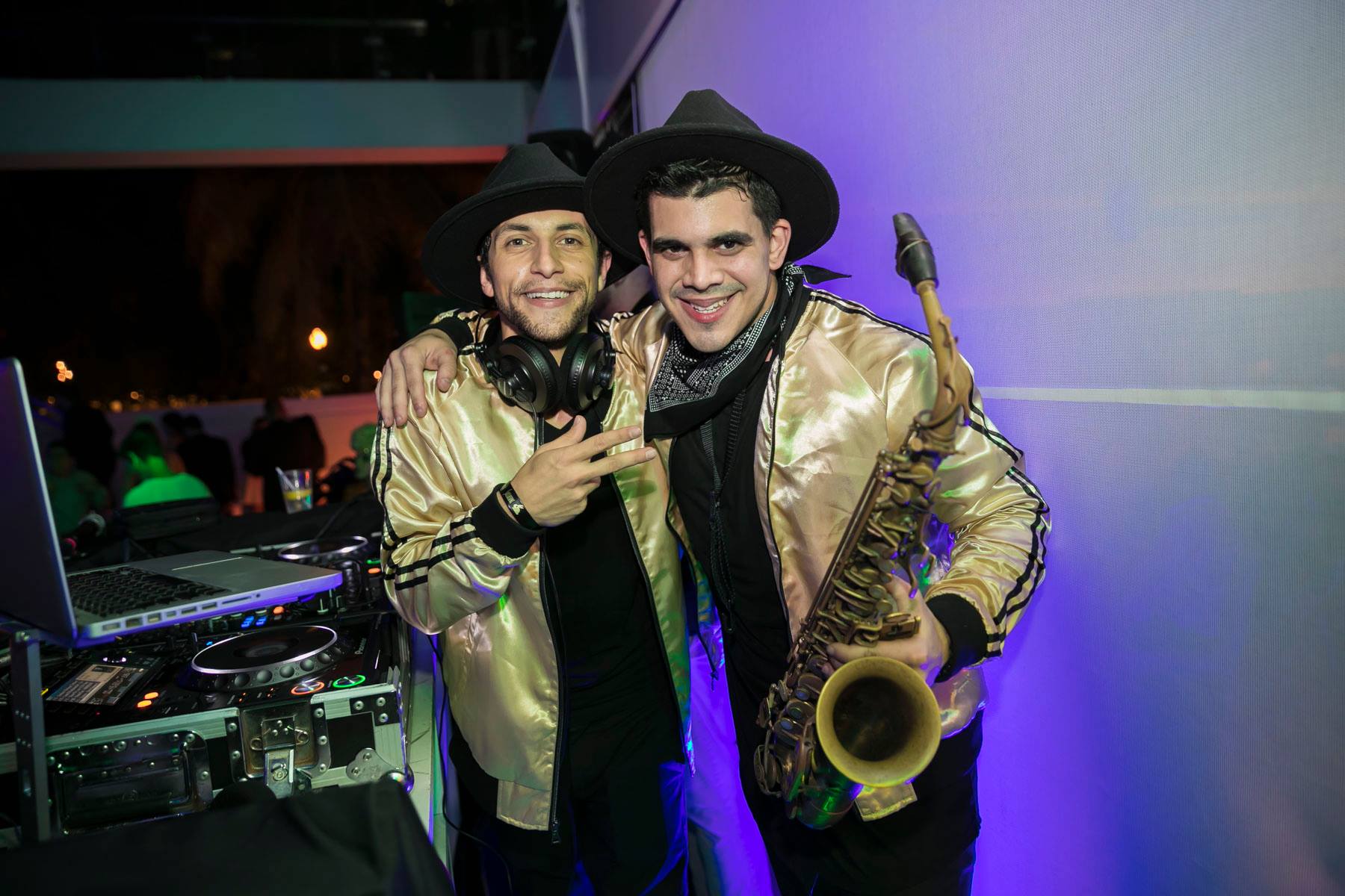 Two performers in gold sequined jackets, one on saxophone, playing the crowd at the DJ booth