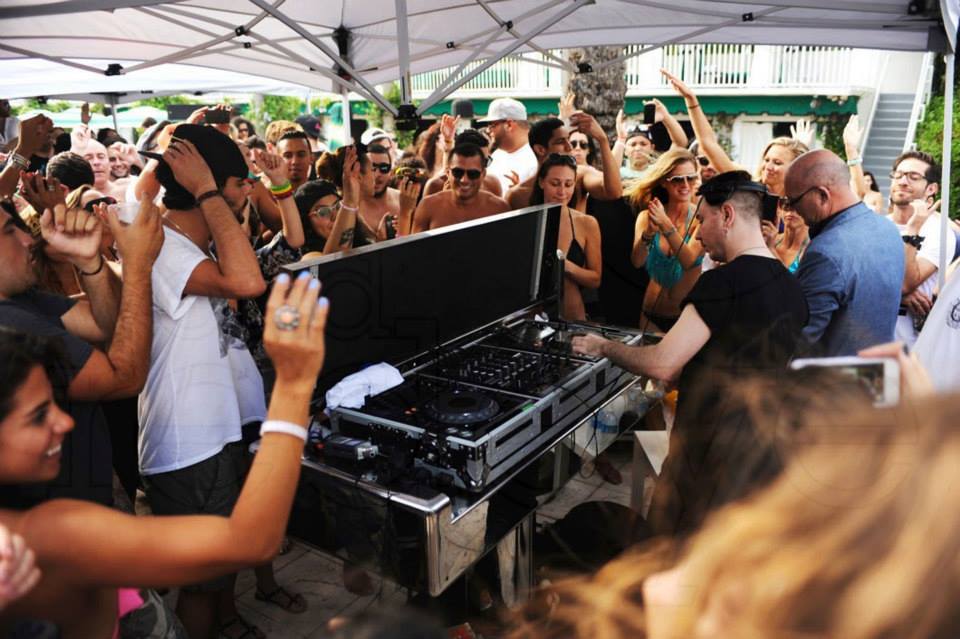DJ playing to a packed daytime crowd with guests filming from the front