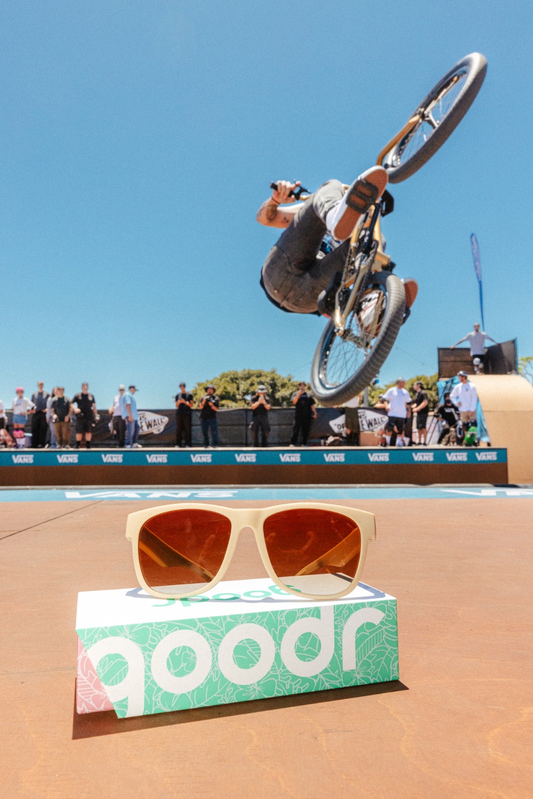 BMX rider inverted mid-air over the ramp behind a pair of goodr shades on a branded box
